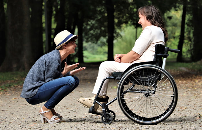 A woman in a wheelchair kneels to engage in conversation with another man, presents connection and support